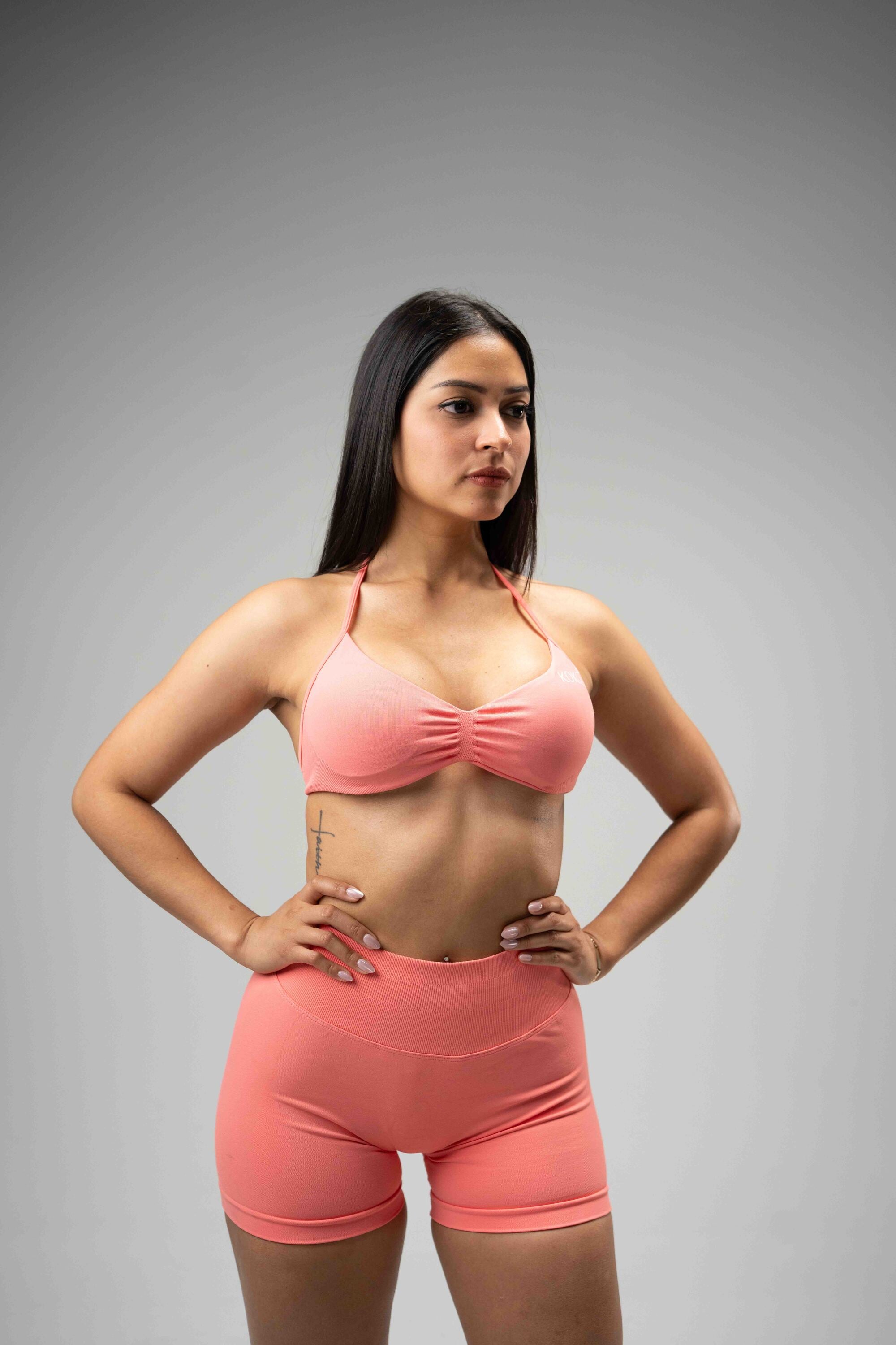 Woman wearing a pink sports bra and shorts on a gray background